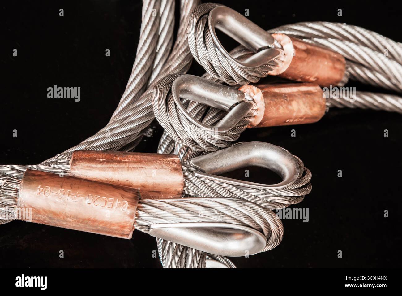 Câble en acier inoxydable, avec boucles et pinces en cuivre, et un fond noir, gros plan. Banque D'Images