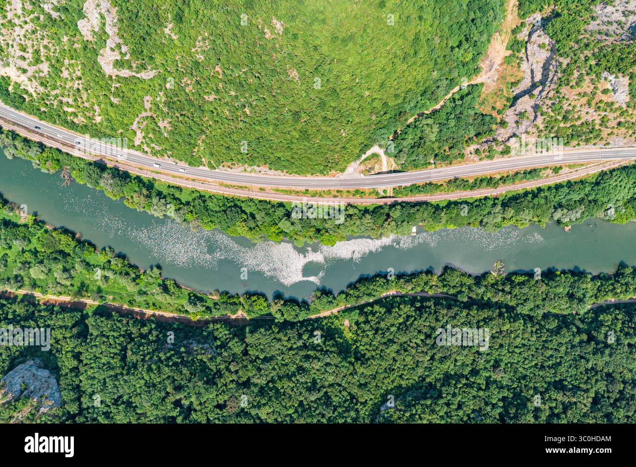 Capture d'une vue aérienne de voitures voyageant le long d'une autoroute à côté d'une rivière sinueuse et d'un chemin de fer, niché dans une vallée verdoyante avec des forêts Banque D'Images