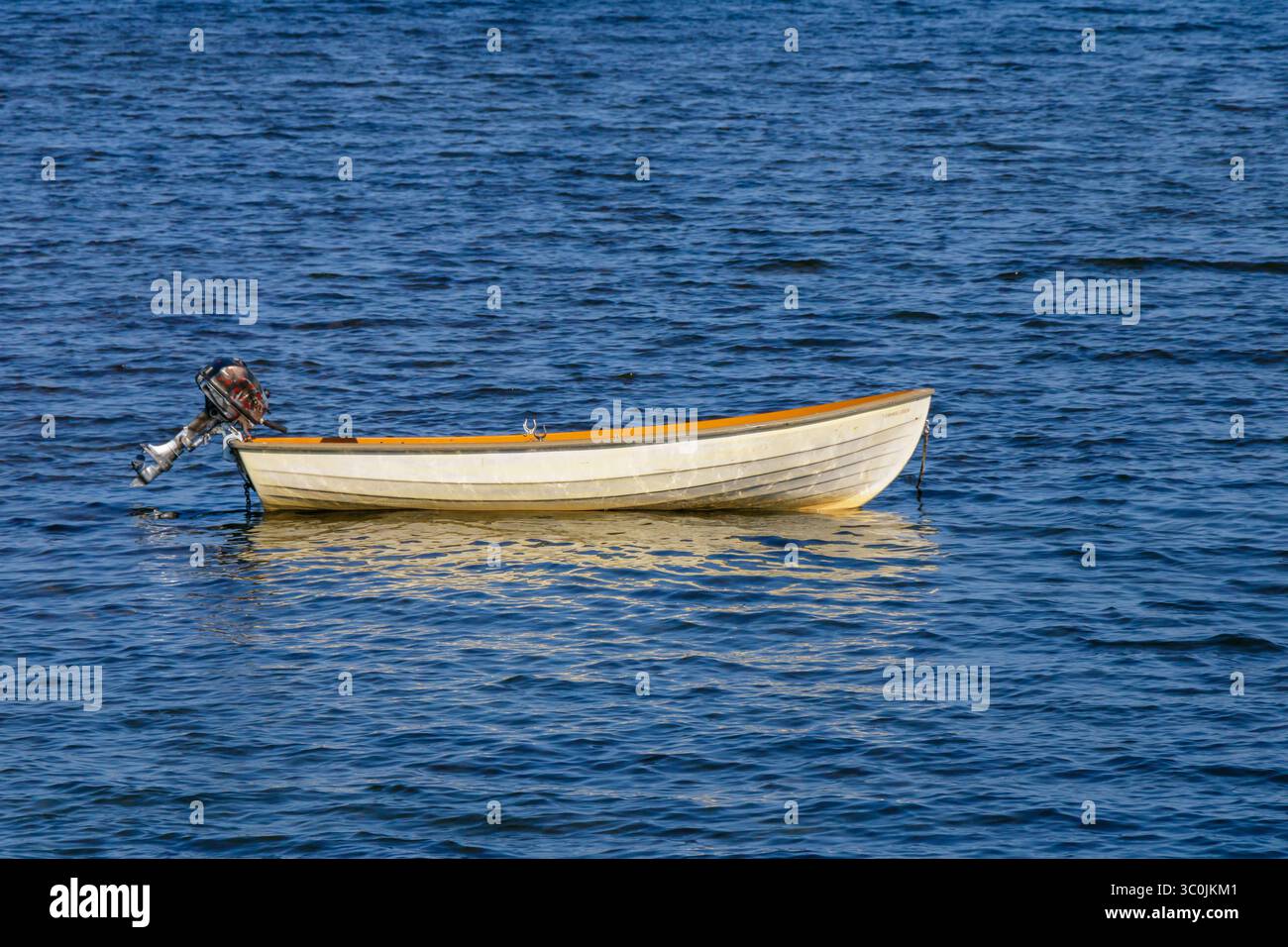 Un petit bateau à moteur repose calmement à la surface des eaux bleues, reflétant la lumière du soleil, entouré d'une atmosphère sereine. L'environnement suggère un calme Banque D'Images