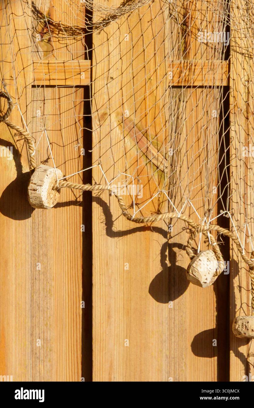 Un filet de pêche orné de flotteurs se drape sur un mur en bois altéré, créant une esthétique côtière. La lumière chaude du soleil met en valeur la texture et le colo Banque D'Images
