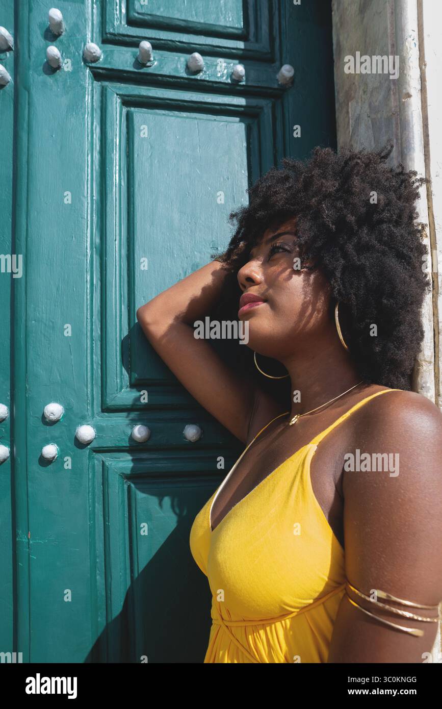 Belle femme noire avec des cheveux de corbeau portant une robe jaune posant pour la photo contre la grande porte verte de l'église. Heureux et souriant Banque D'Images