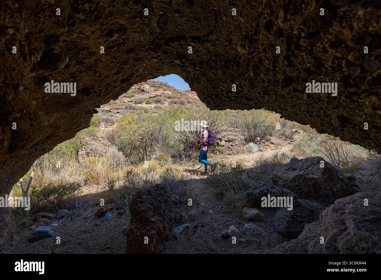 Randonneuse femme marchant devant l'entrée d'une grotte volcanique dans un paysage de canyon sec Banque D'Images