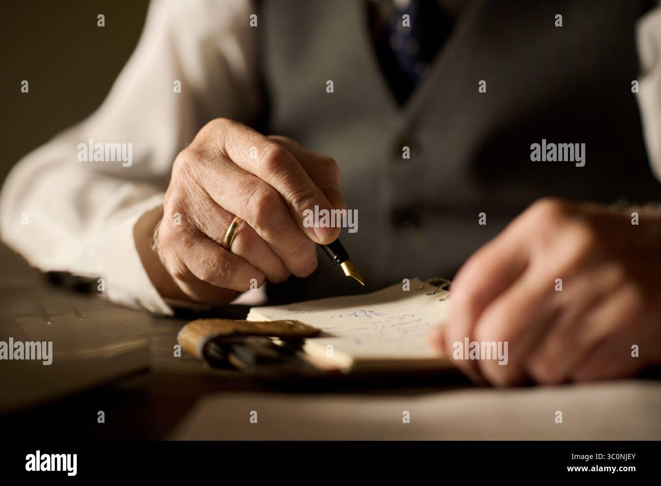 Homme d'âge moyen caucasien écrivant avec un stylo plume sur le bloc-notes, gros plan des mains montrant une bague de mariage en or et une tenue formelle, capturant les détails du travail professionnel ou personnel Banque D'Images