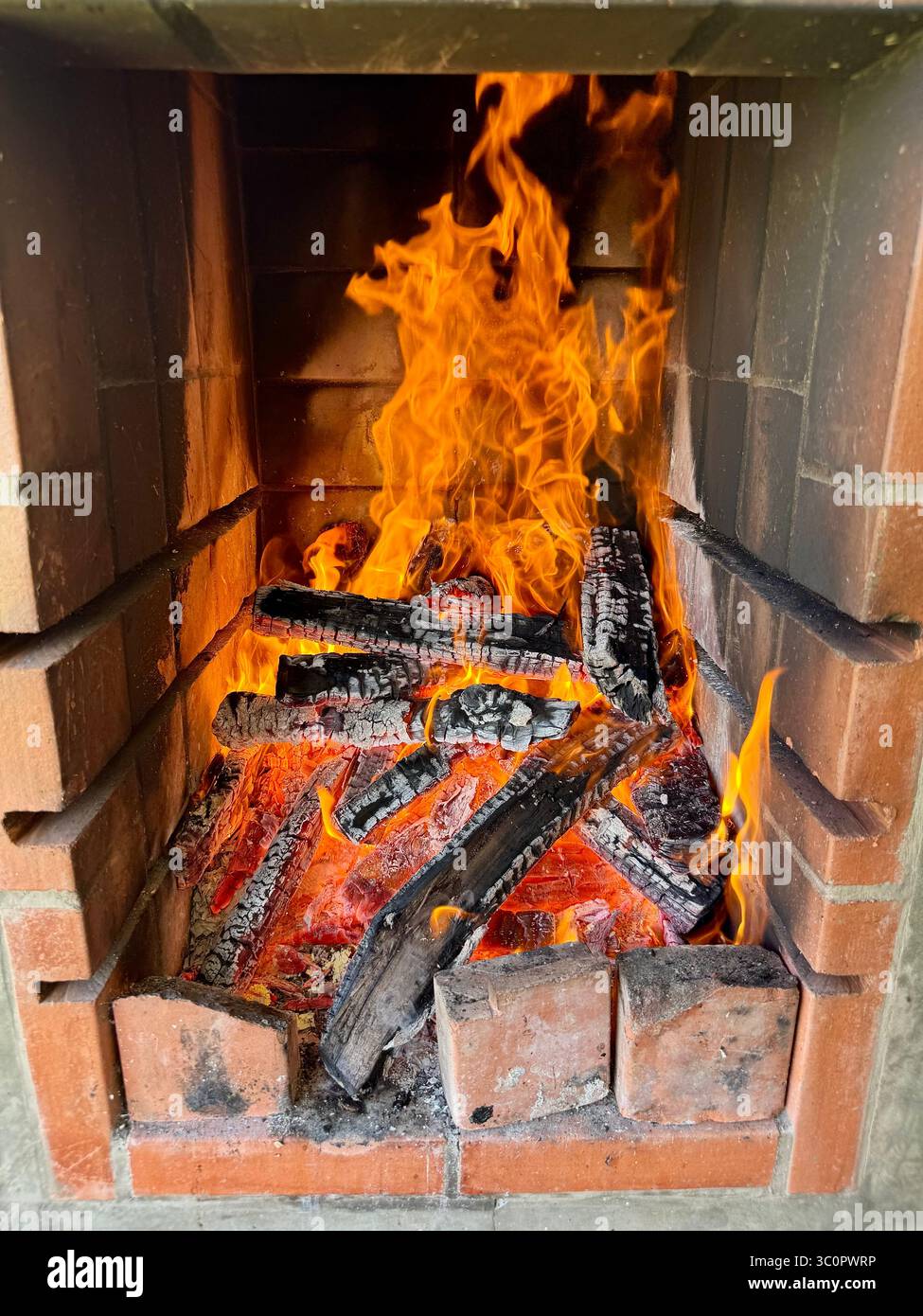 Flammes et braises incandescentes dans une cheminée en brique avec des bûches de bois brûlantes pour barbecue Banque D'Images