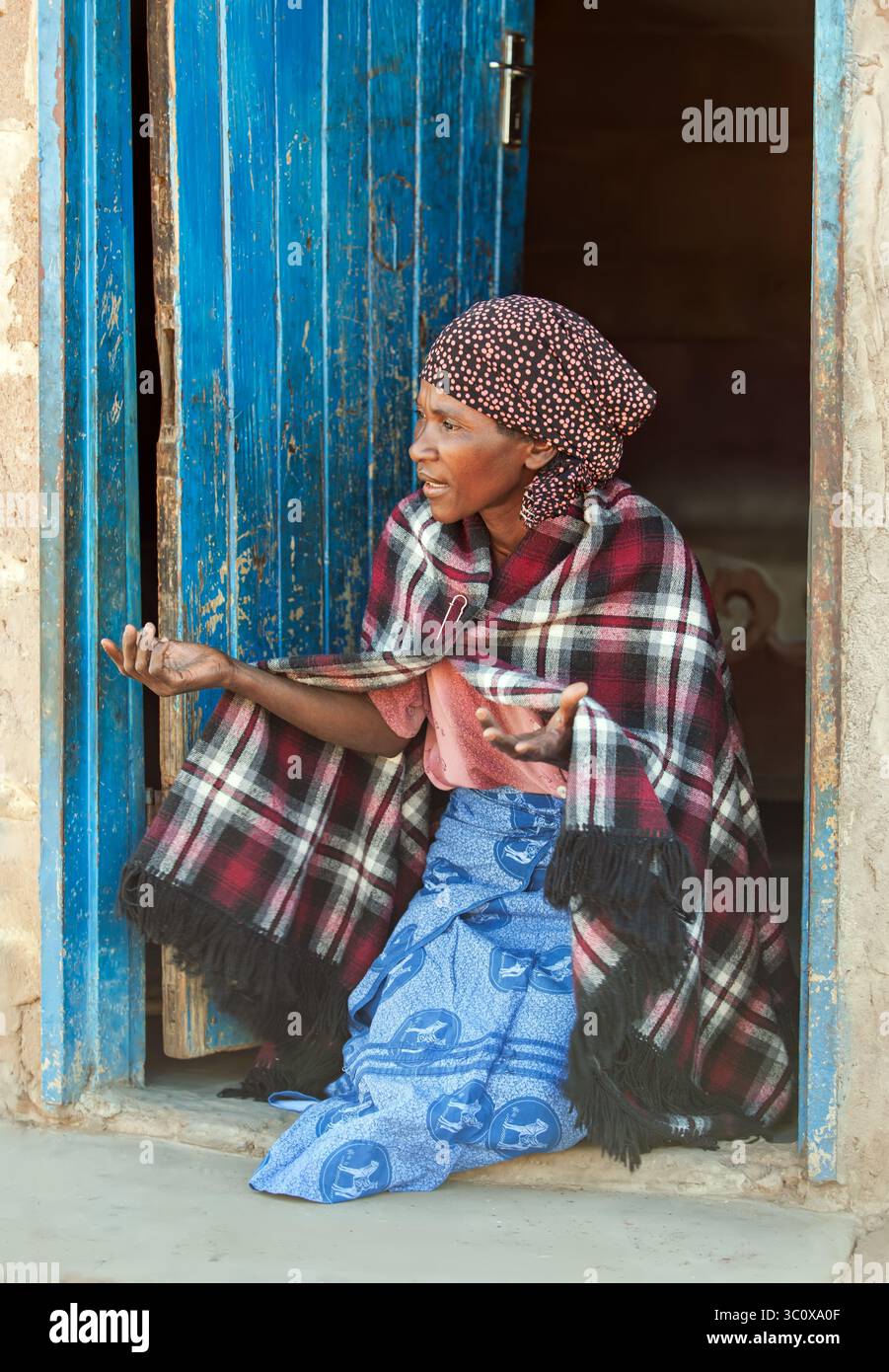 religion dans le village, femme africaine religieuse agenouillée dans la porte priant, devant la rondavelle de la cabane au toit de chaume Banque D'Images