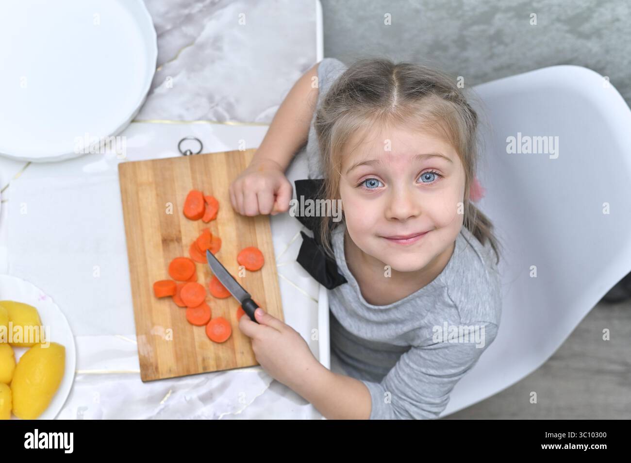 L'aide de cuisine affiche fièrement ses résultats de coupe de carottes. Parfait pour le contenu sur l'encouragement de la participation des enfants aux tâches ménagères. pour fami Banque D'Images