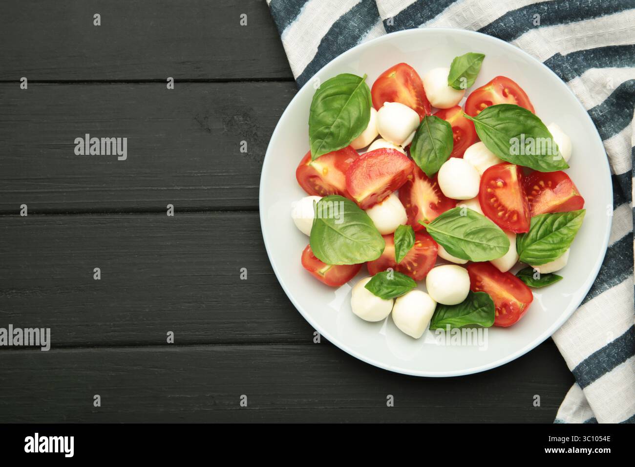 Salade Caprese italienne avec tomates cerises, mozzarella, basilic sur assiette sur fond noir. Vue de dessus Banque D'Images