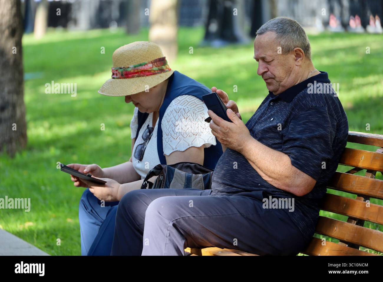 Moscou, Russie - 18 juillet 2025 : vieux couple assis sur un banc dans un parc d'été. Homme et femme utilisant des smartphones, la vie à la retraite Banque D'Images