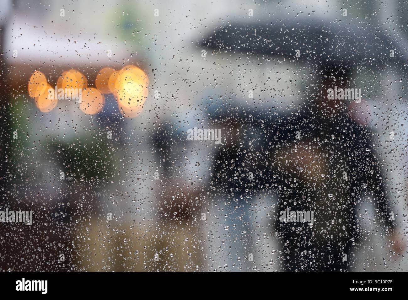 Pluie abondante dans une ville, vue défocalisée à travers le verre humide avec des gouttes d'eau aux gens marchant avec des parapluies Banque D'Images