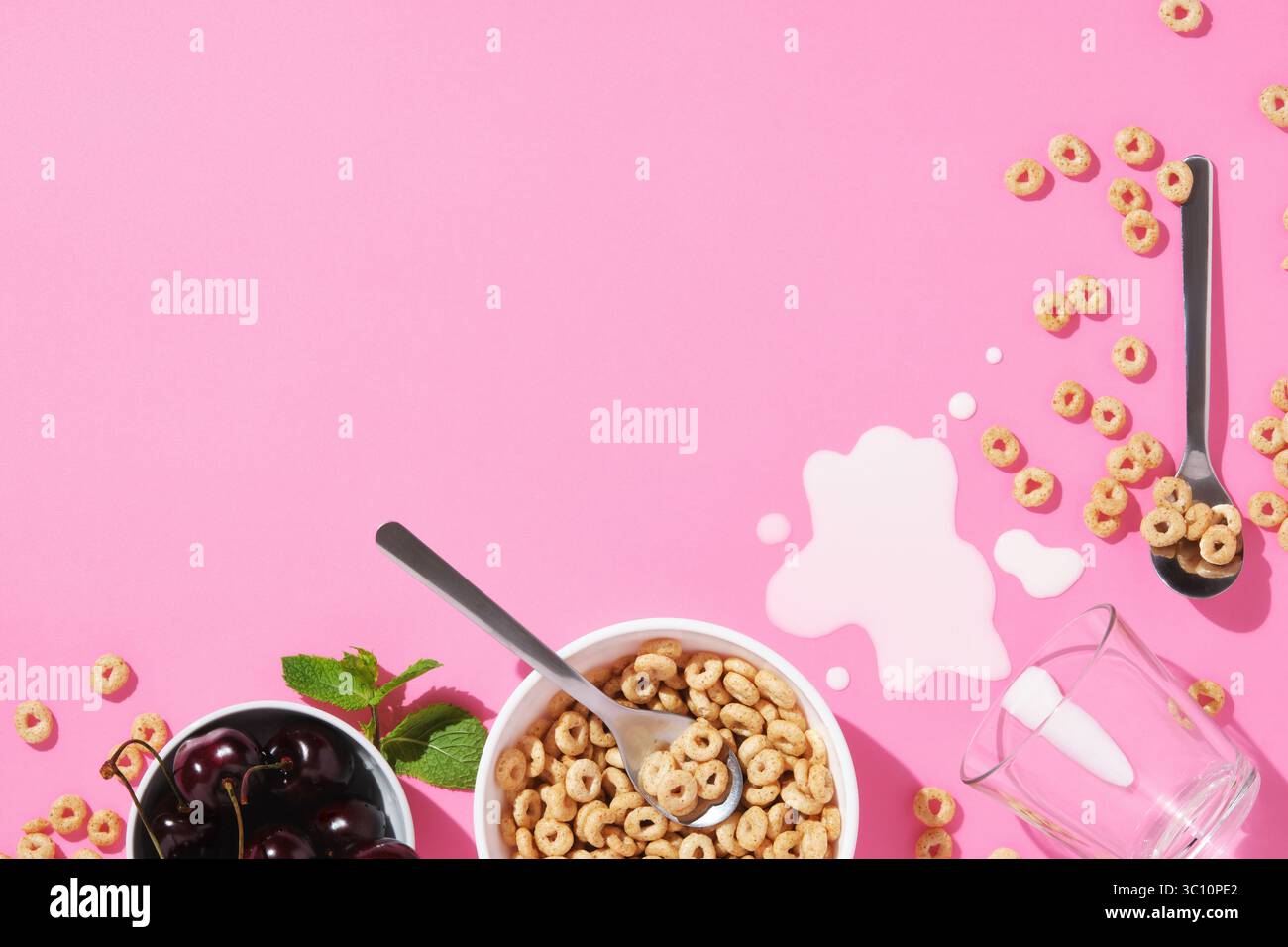 Anneaux de petit déjeuner, cerises, feuilles de menthe, une cuillère, lait renversé, et un bol sur fond rose. Concept du matin avec espace pour votre texte. Banque D'Images Anneaux de petit déjeuner, cerises, feuilles de menthe, une cuillère, lait renversé, et un bol sur fond rose. Concept du matin avec espace pour votre texte. Banque D'Images