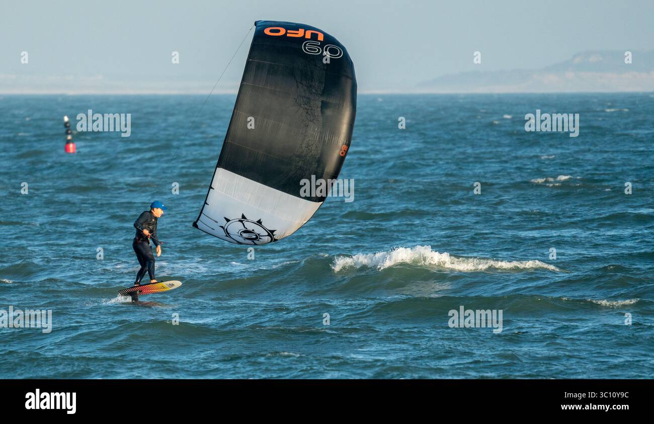 Cerf-volant solitaire mâle, kitesurfeur, en pleine voile dans l'eau au large d'Avon Beach dans le Dorset, Angleterre, Royaume-Uni Banque D'Images
