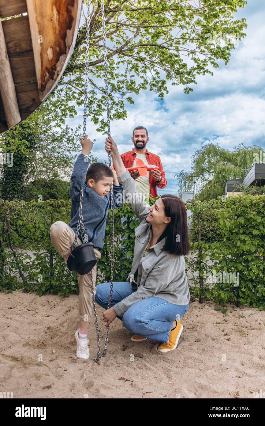 Famille multinationale avec garçon de 6 ans jouant ensemble à l'aire de jeux. Parents impliqués dans la parentalité active, construisant de solides relations avec les enfants Thr Banque D'Images