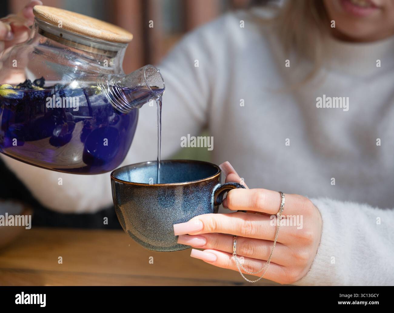 Une femme verse du thé bleu dans une tasse élégante, capturant un moment de bonheur de détente et de tranquillité Banque D'Images