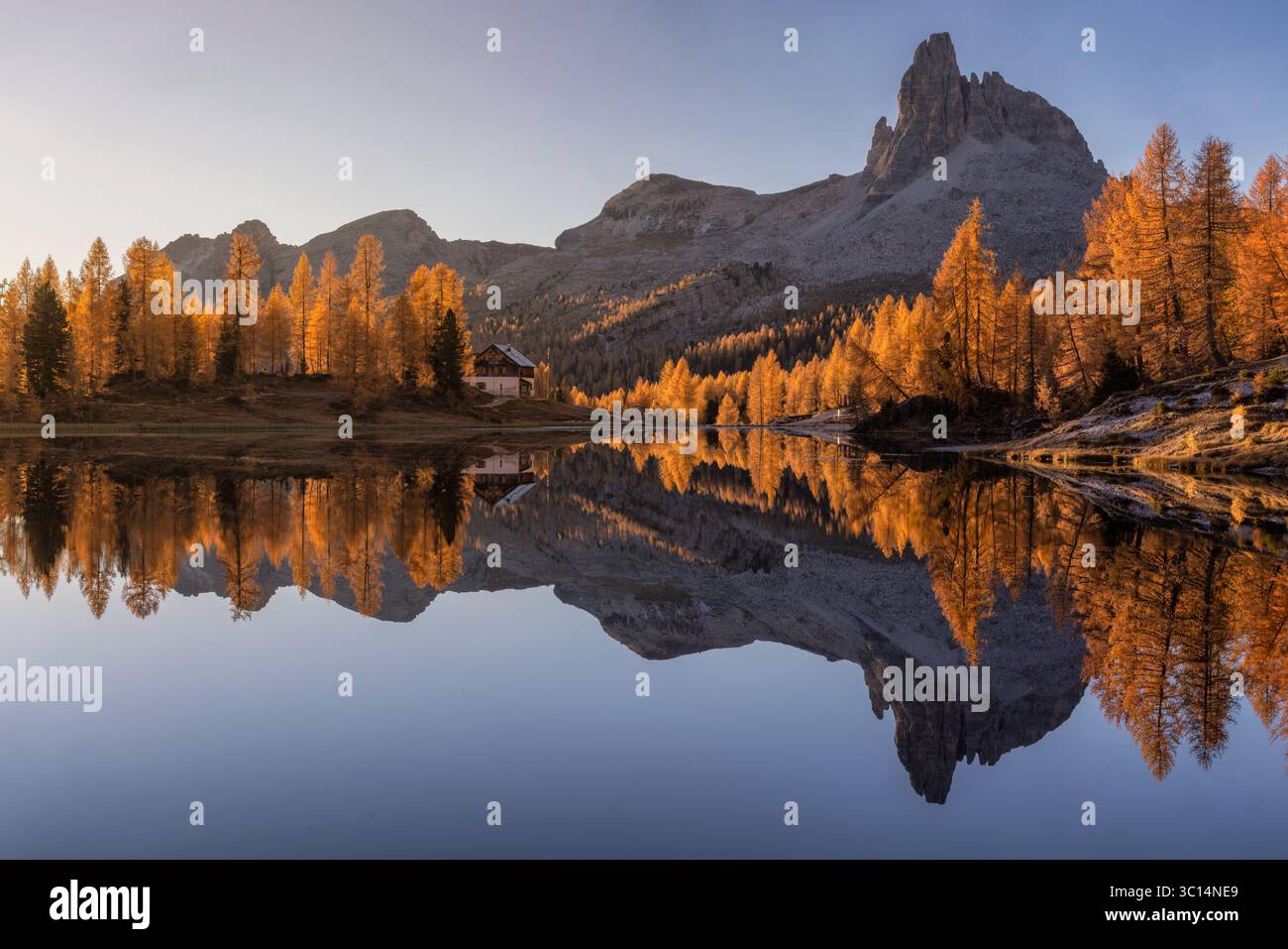 Vue sur les mélèzes dorés reflétant dans le lac calme, une maison rustique nichée sous l'imposant lac Federa Italie. Banque D'Images