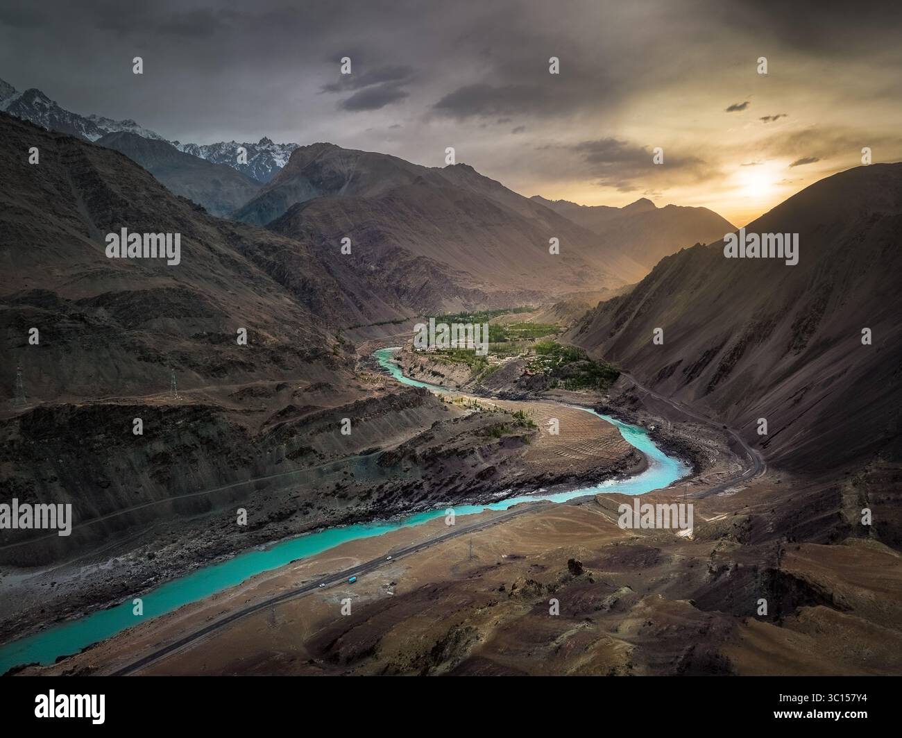 Vue aérienne de la rivière Shyok serpentant à travers le paysage accidenté et aride, contrastant fortement avec les sommets enneigés sous un ciel spectaculaire, Ladakh, Inde. Banque D'Images