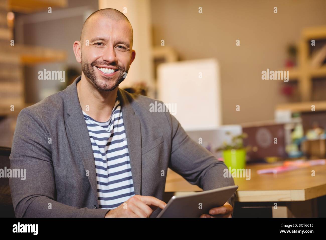 Professionnel assis au bureau tenant une tablette numérique dans un bureau moderne avec ordinateur portable et usine Banque D'Images