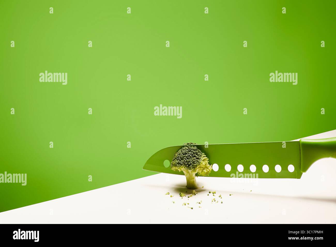 Un couteau vert vif tranche un brocoli miniature, créant une composition surréaliste et artistique. Le brocoli semble sortir Banque D'Images