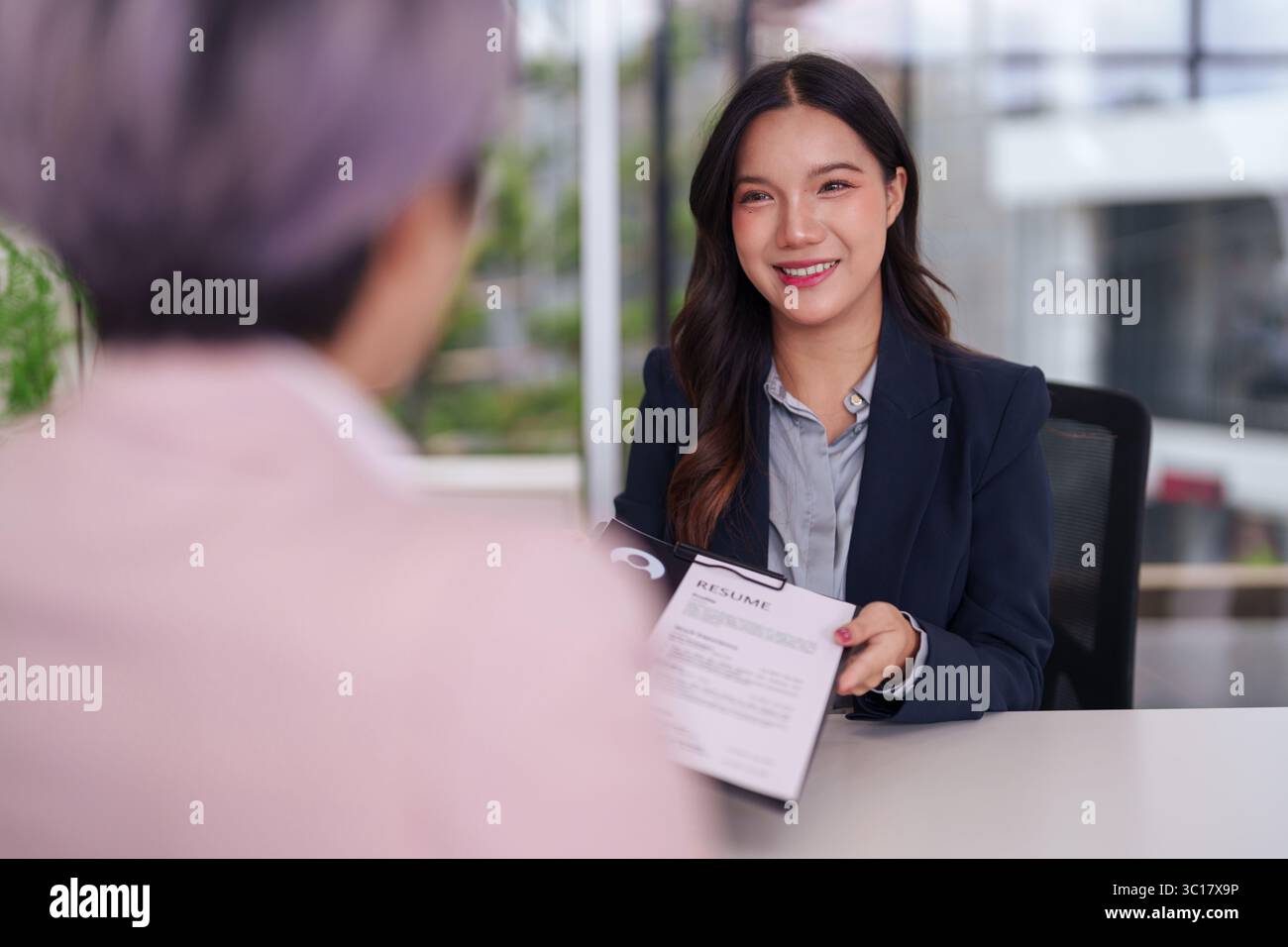 Femme asiatique souriante présente son CV lors d'un entretien d'embauche professionnel. Elle semble confiante et prête pour de nouvelles perspectives de carrière. Banque D'Images