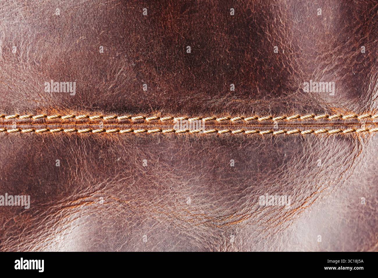 Texture cuir marron gros plan. Couture de fil orange visible. Rides et grain naturels. Détail de la surface du matériau. Artisanat fait main. Banque D'Images