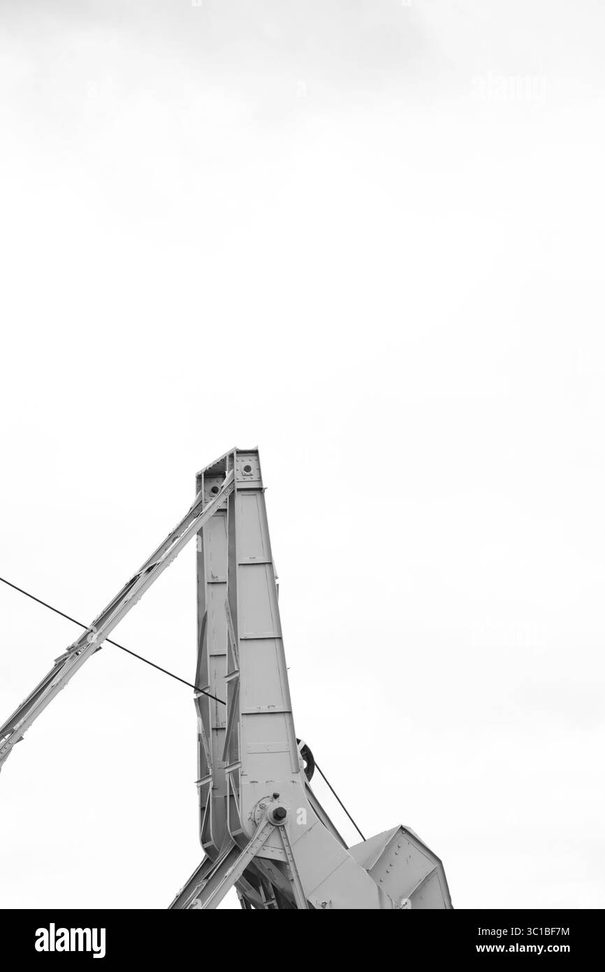 Partie d'une ancienne grue portuaire, petite par rapport à l'immense ciel en arrière-plan, en noir et blanc. Banque D'Images