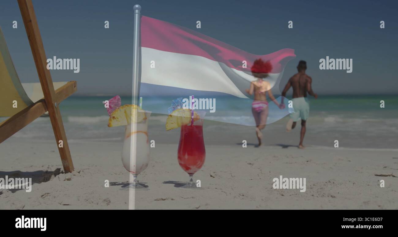 Drapeau rouge blanc bleu agitant sur la plage, avec couple marchant vers le rivage et cocktails près de la chaise Banque D'Images