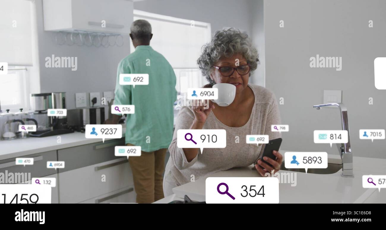 Femme senior vérifiant les notifications de smartphone et tenant la tasse à l'îlot de cuisine, superpositions numériques Banque D'Images