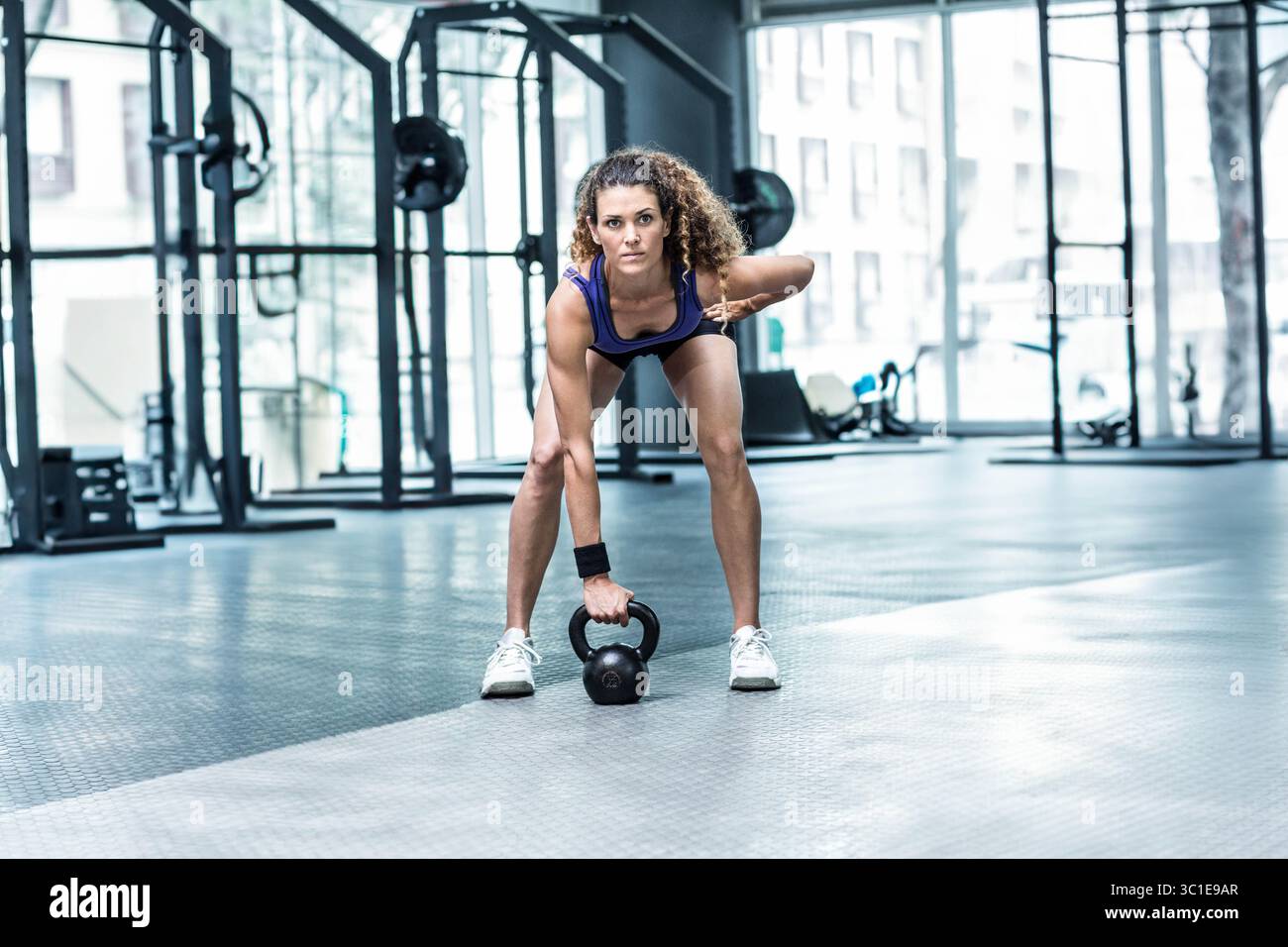 Femme passionnée de fitness portant un débardeur bleu soulevant kettlebell noir tout en se penchant dans la salle de gym Banque D'Images