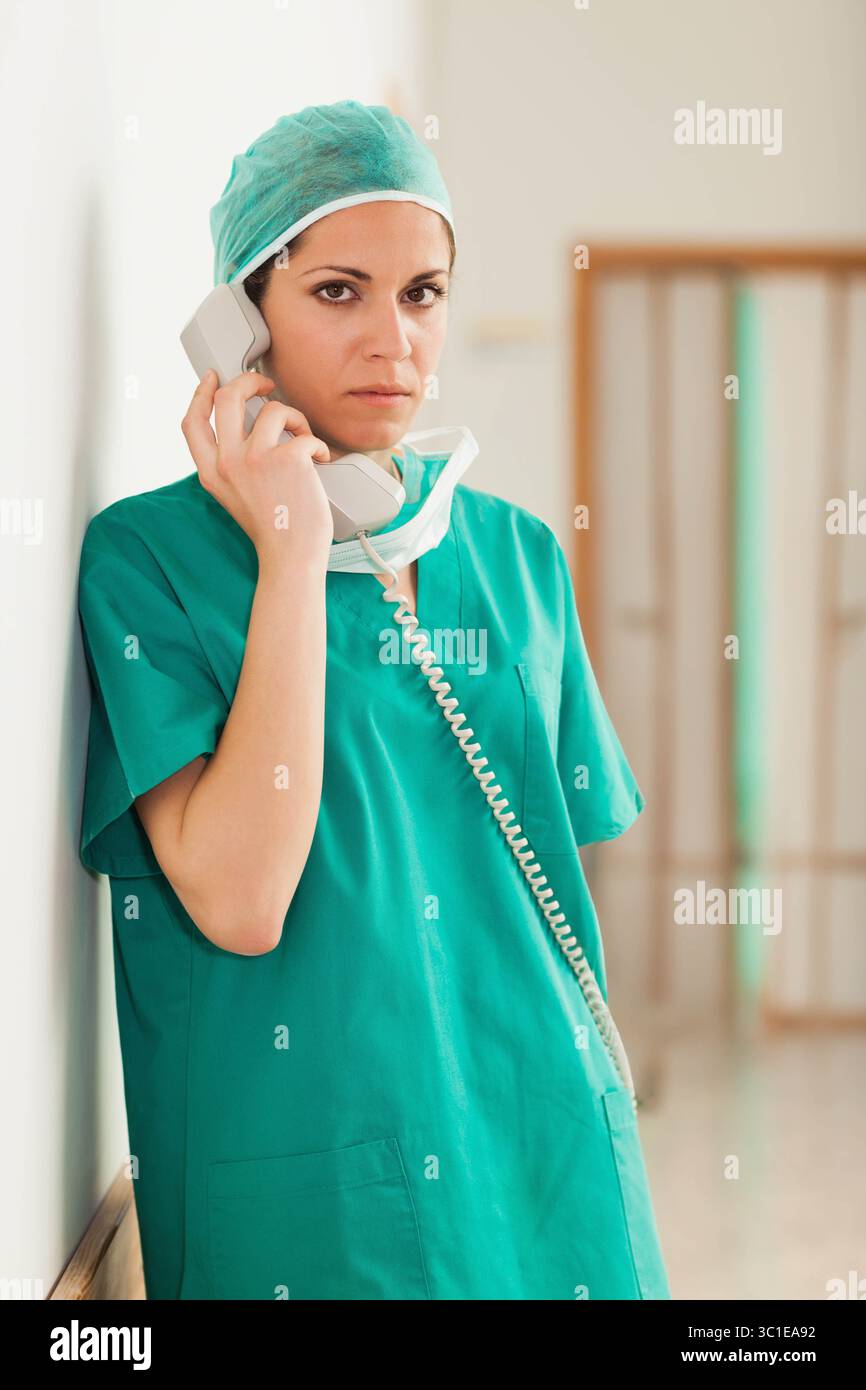 Chirurgien féminin portant des gommages verts parlant au téléphone filaire dans le couloir de l'hôpital, espace de copie Banque D'Images