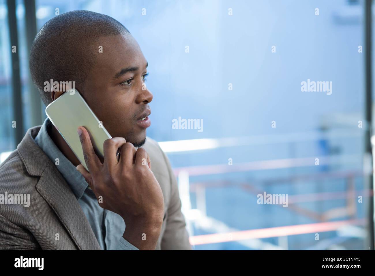 Homme afro-américain en blazer tenant smartphone à l'oreille par balustrade en verre dans le bureau, espace de copie Banque D'Images