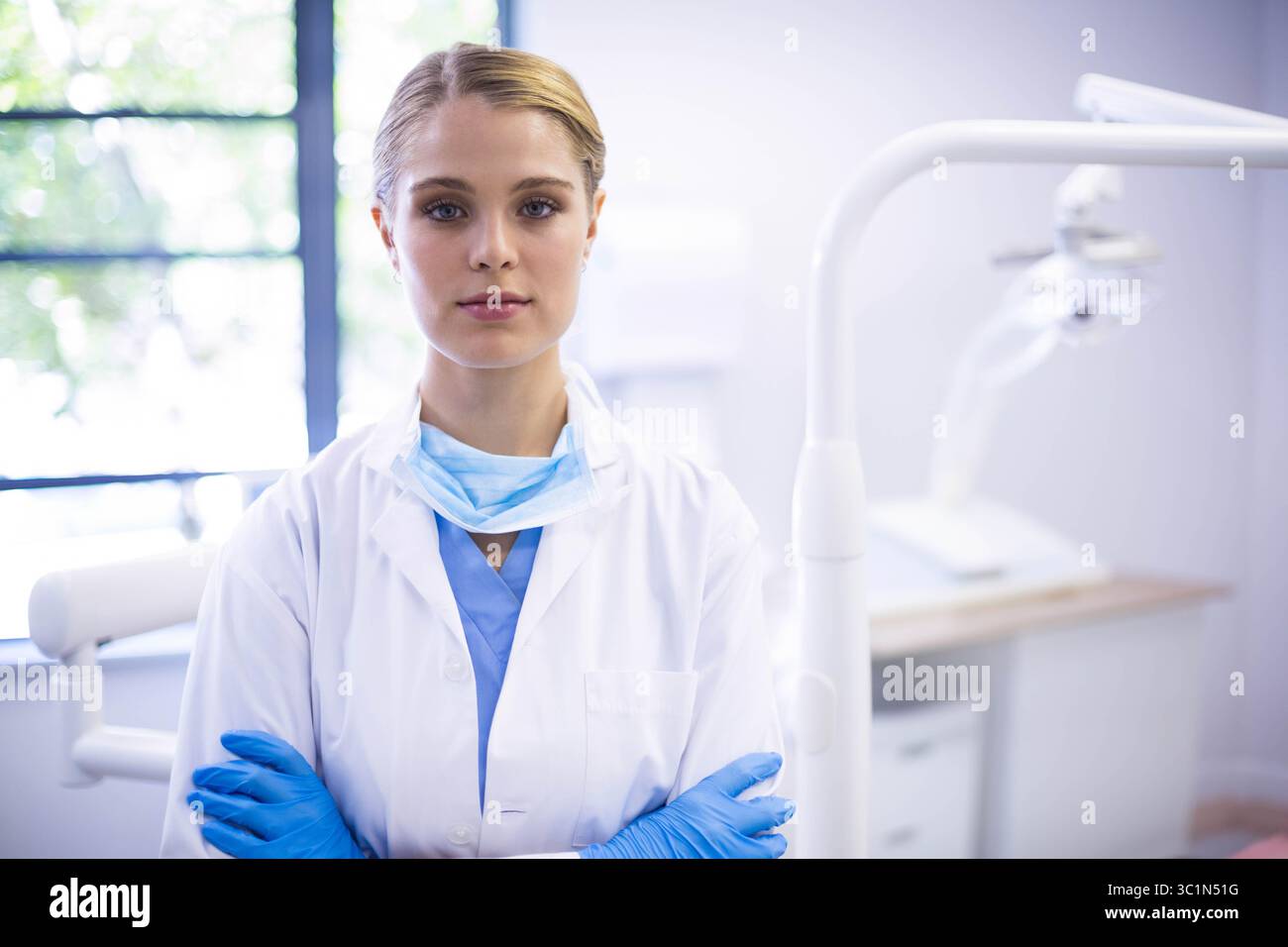 Dentiste adulte femme debout avec les bras croisés dans une clinique dentaire près de la fenêtre et du plafonnier Banque D'Images