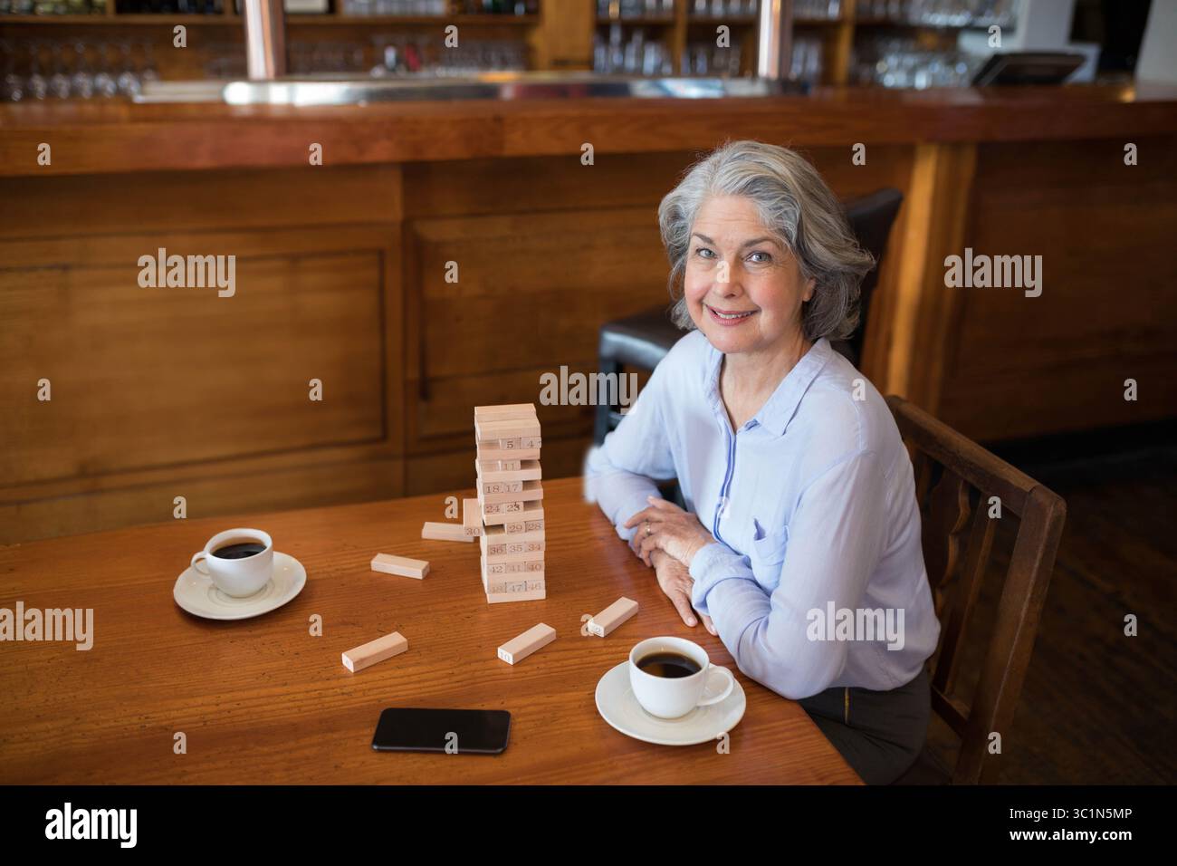 Femme senior assise dans la tour de bloc de construction de café avec tasses à café et smartphone souriant à la caméra Banque D'Images