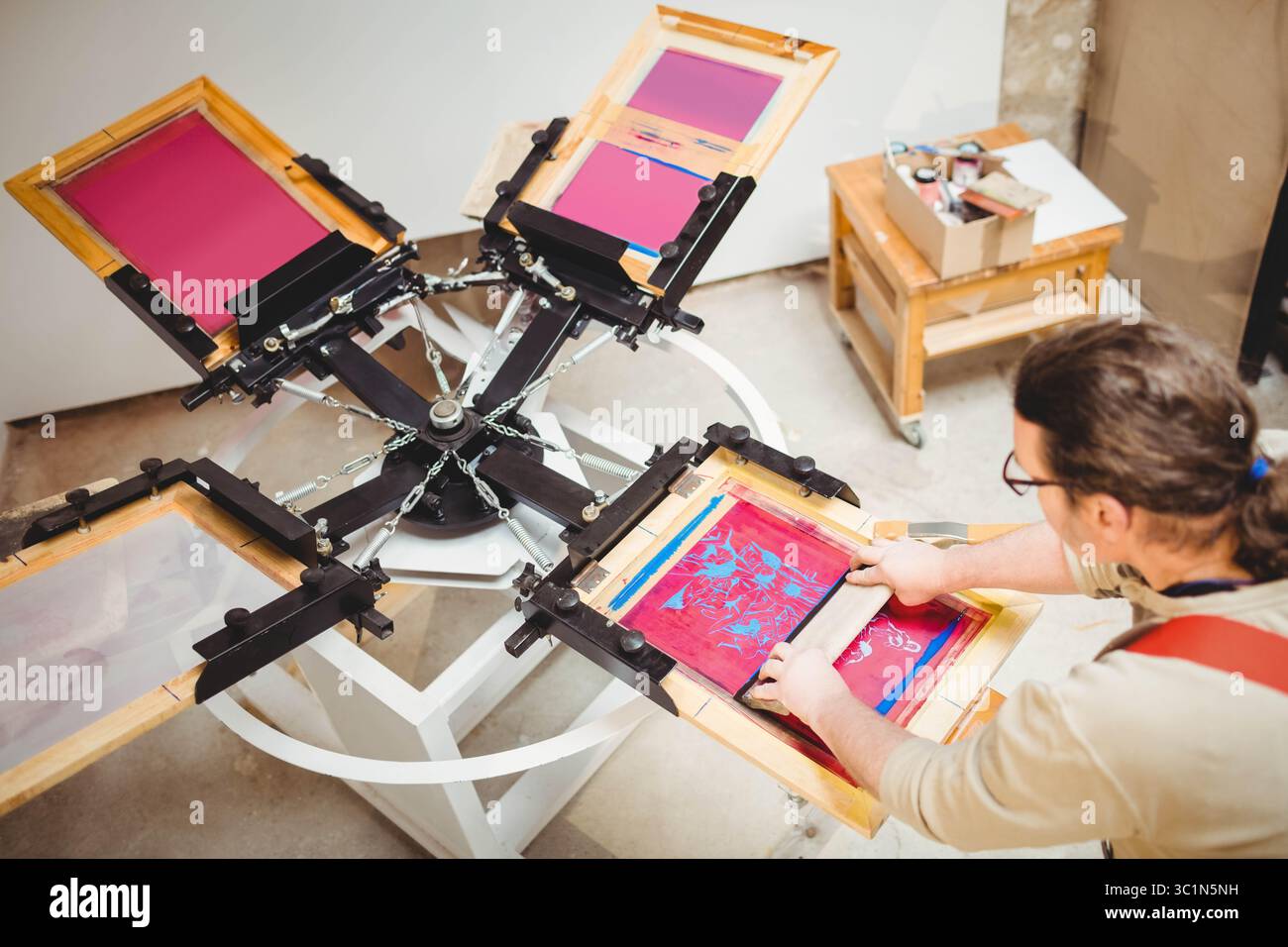 Presse de sérigraphie tournant sur carrousel dans le studio distribuant des encres sur les écrans et le chariot d'approvisionnement Banque D'Images