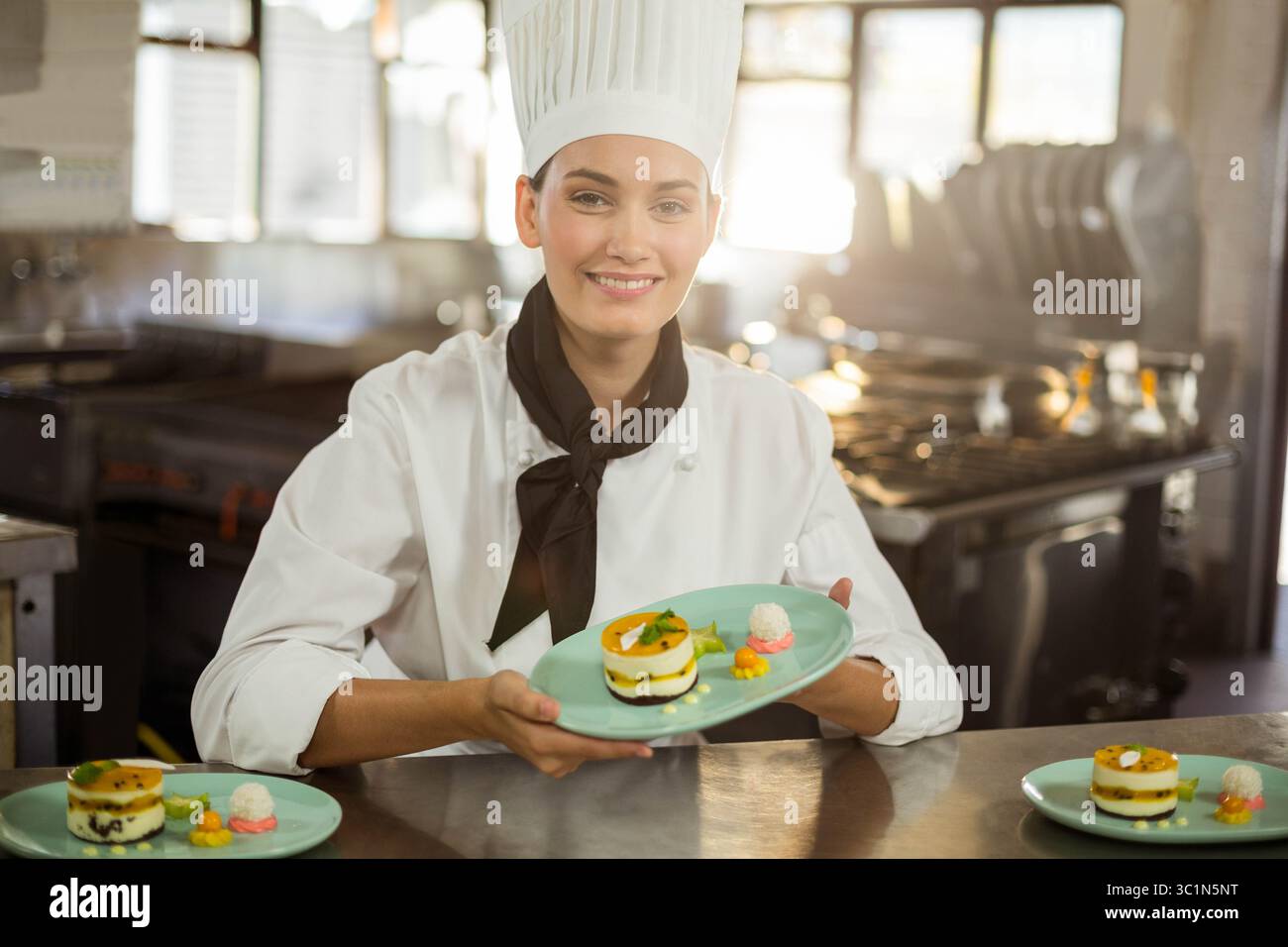 Femme chef dans le placage uniforme des desserts superposés avec garniture de fruits sur le comptoir dans la cuisine avec des fours Banque D'Images