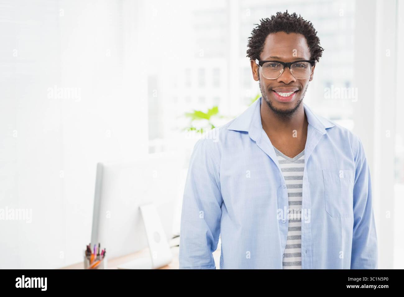 Homme afro-américain travaillant sur ordinateur dans l'espace de travail de bureau avec tasse à crayon et plante, espace de copie Banque D'Images