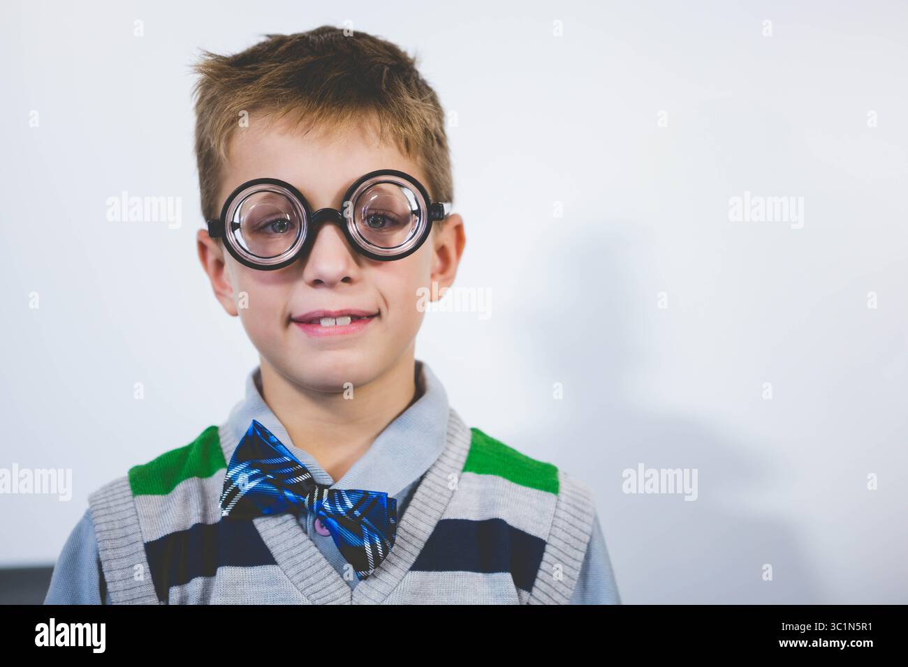 Garçon d'âge scolaire posant contre le mur du studio portant gilet de pull rayé gilet de fantaisie lunettes et noeud papillon Banque D'Images