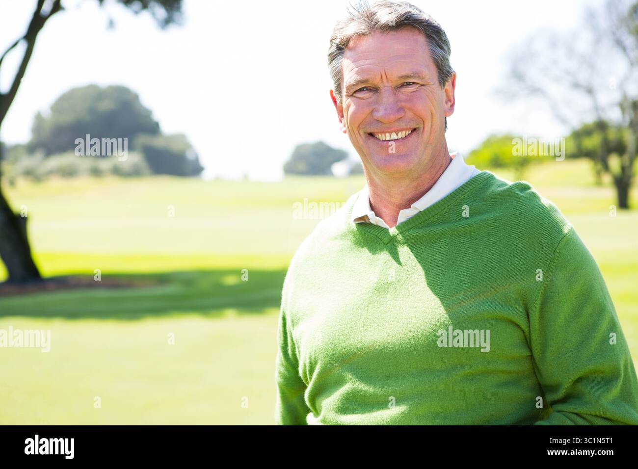 Homme afro-américain senior debout sur le terrain de golf portant un pull vert, chemise blanche, espace de copie Banque D'Images