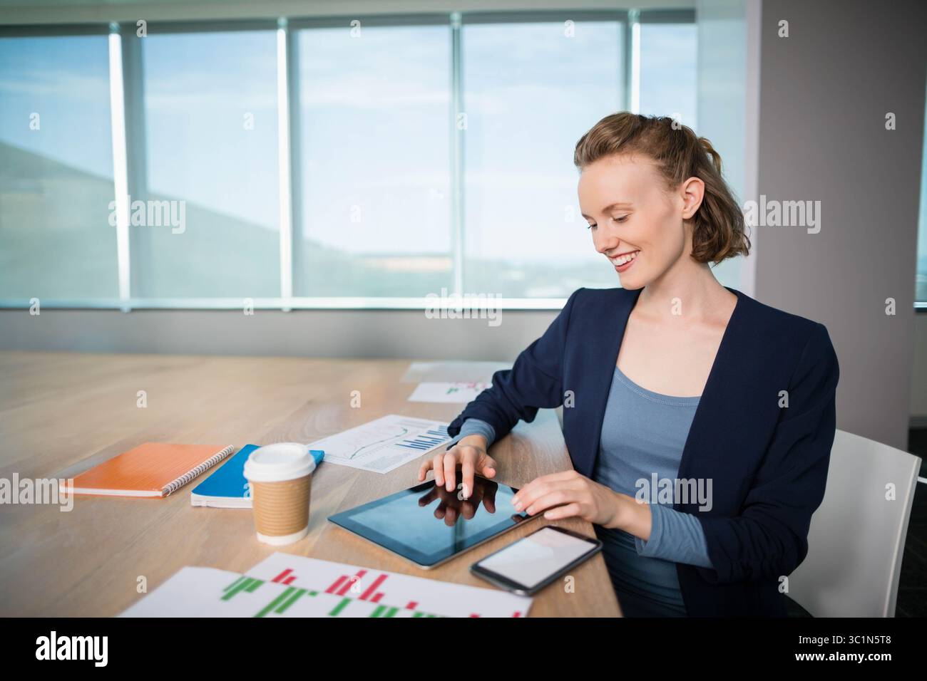 Tablette de tapotement professionnelle d'affaires à la table de réunion en bois avec graphiques, smartphone et vue sur les collines Banque D'Images
