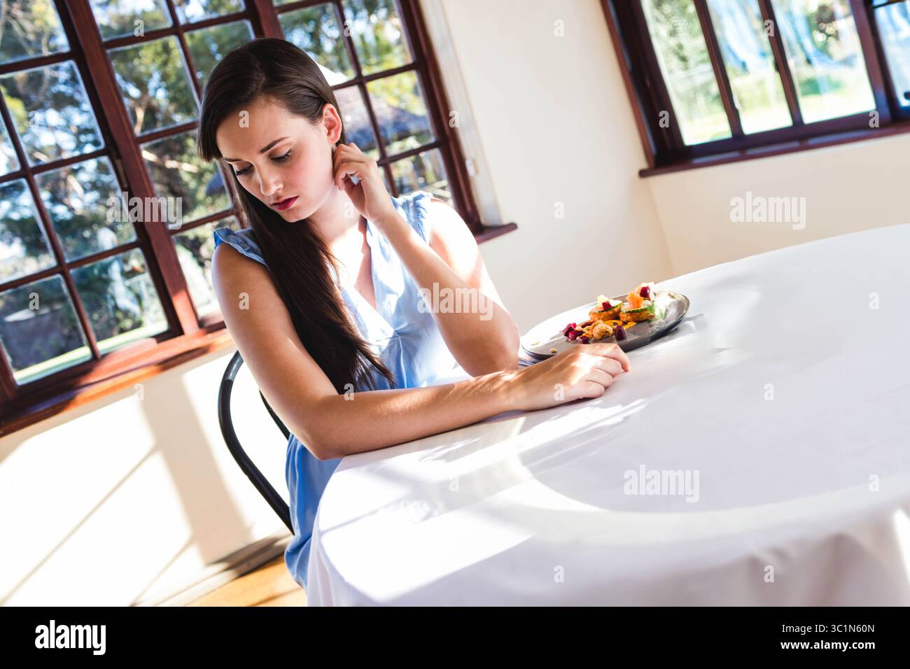 Femme assise à la table ronde en tissu blanc par des fenêtres en bois, dégustation de pâtisseries et de fruits, espace copie Banque D'Images