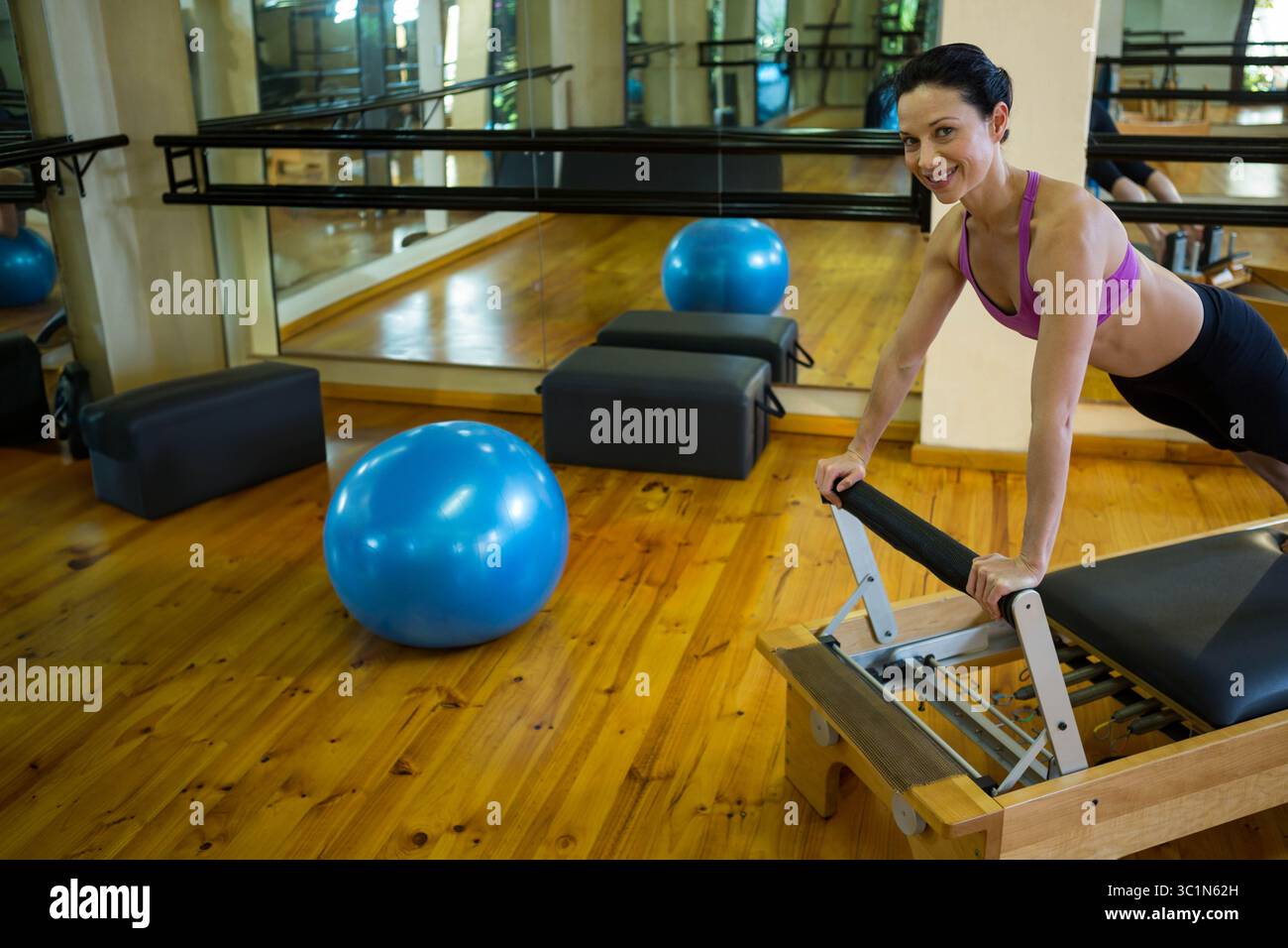 Machine de reformage Pilates montrant des mouvements d'étirement sur le sol en pin, avec ballon d'exercice bleu à proximité Banque D'Images