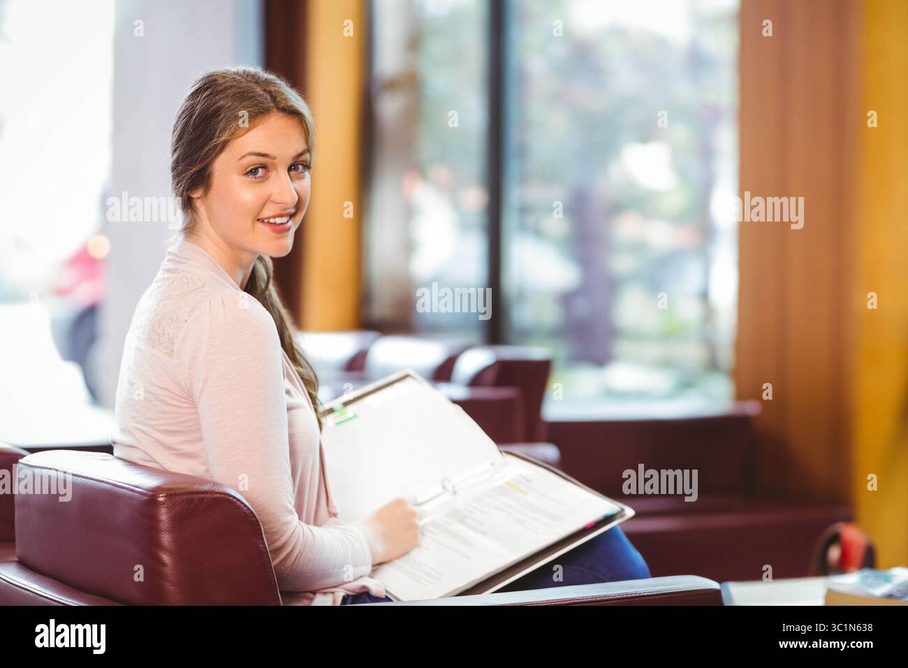 Femme lisant le classeur ouvert tout en étant assise sur la chaise longue en cuir dans la zone d'étude, espace de copie Banque D'Images