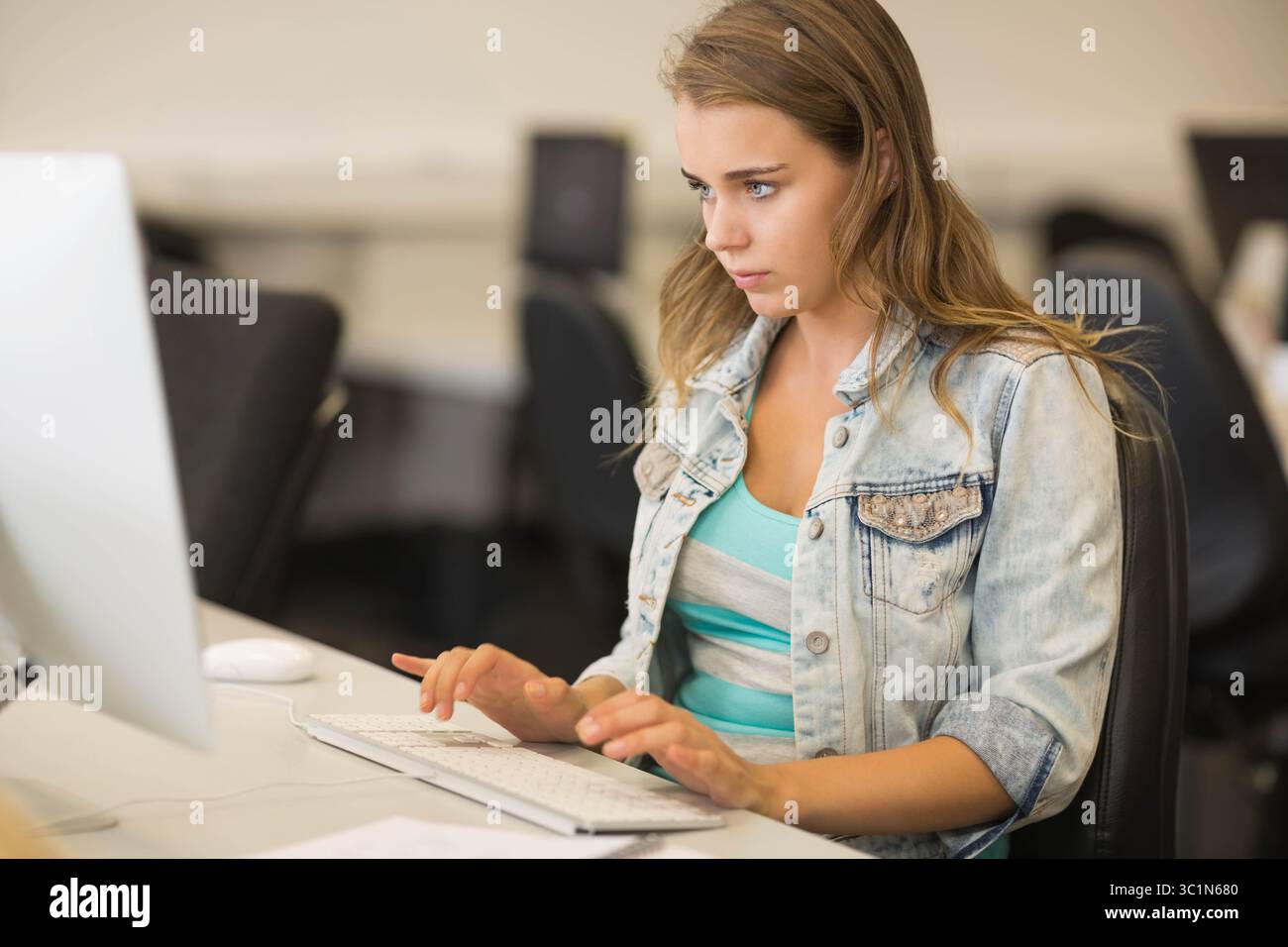 Femme tapant sur le clavier externe au poste de travail de laboratoire informatique portant une veste en denim et un haut rayé Banque D'Images