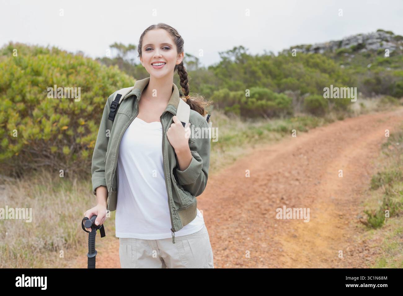 Femme randonneur tenant le bâton de trekking tout en ajustant le sac à dos sur le sentier de terre enroulé, espace de copie Banque D'Images