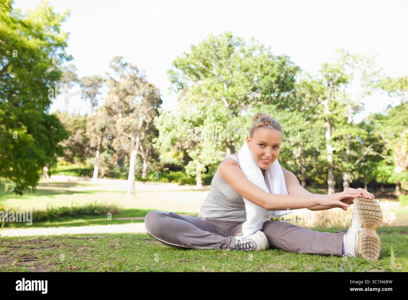 Femme chevauchant la pelouse herbeuse dans le parc portant des vêtements de sport gris avec serviette blanche et chaussures Banque D'Images