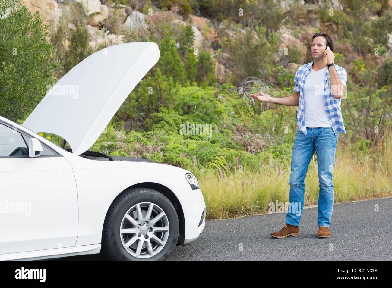 Homme tenant smartphone et faisant des gestes à côté du capot ouvert berline blanche sur le bord de la route, espace de copie Banque D'Images