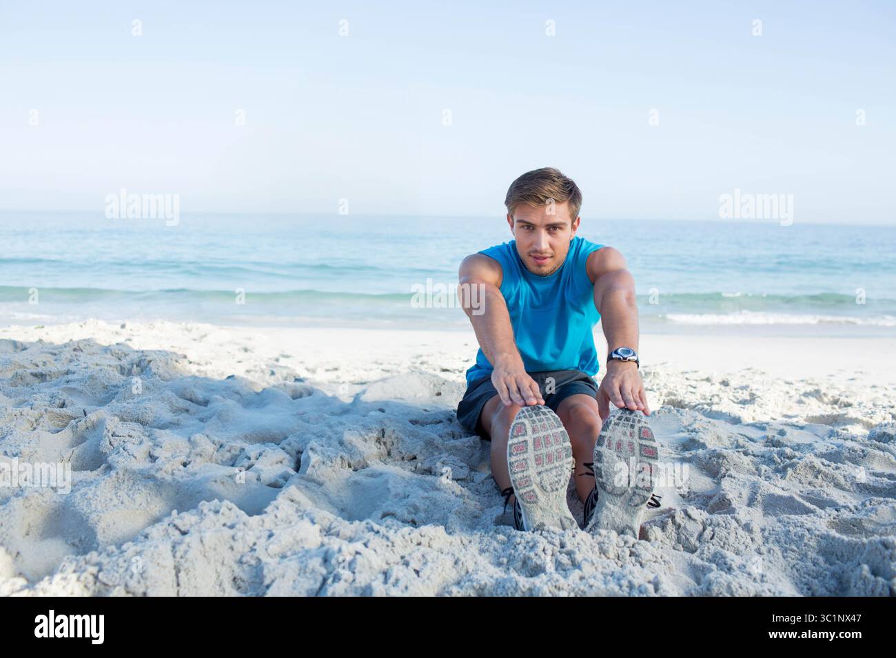 Athlète masculin s'étirant vers l'avant sur le rivage, portant une montre de sport et des chaussures de course Banque D'Images