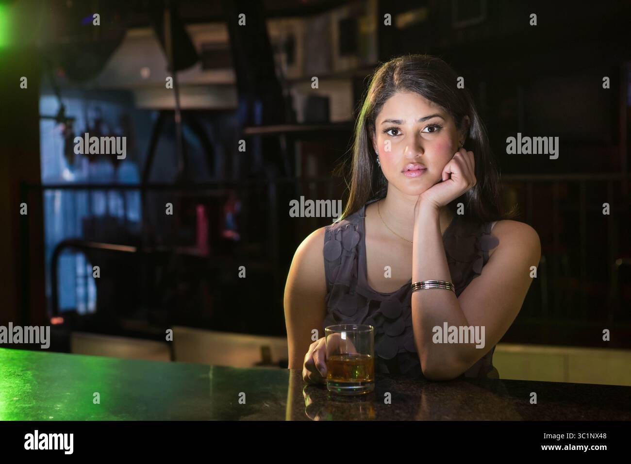 Femme sud-asiatique reposant joue sur la main assise au comptoir du bar tenant le verre de gobelet, espace de copie Banque D'Images