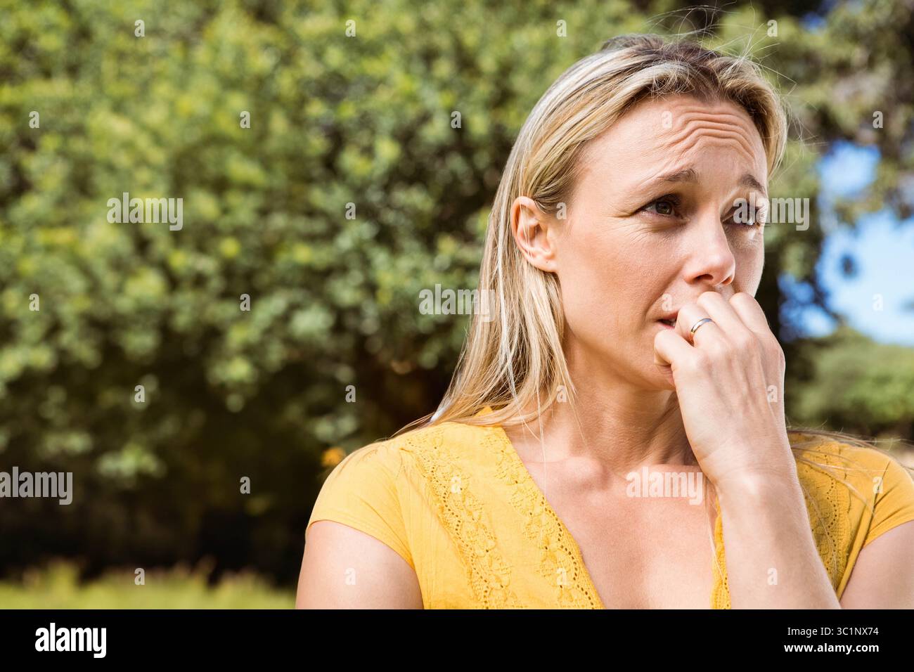 Femme d'âge moyen mordant les ongles au parc portant un haut en dentelle jaune avec bague en argent, espace de copie Banque D'Images