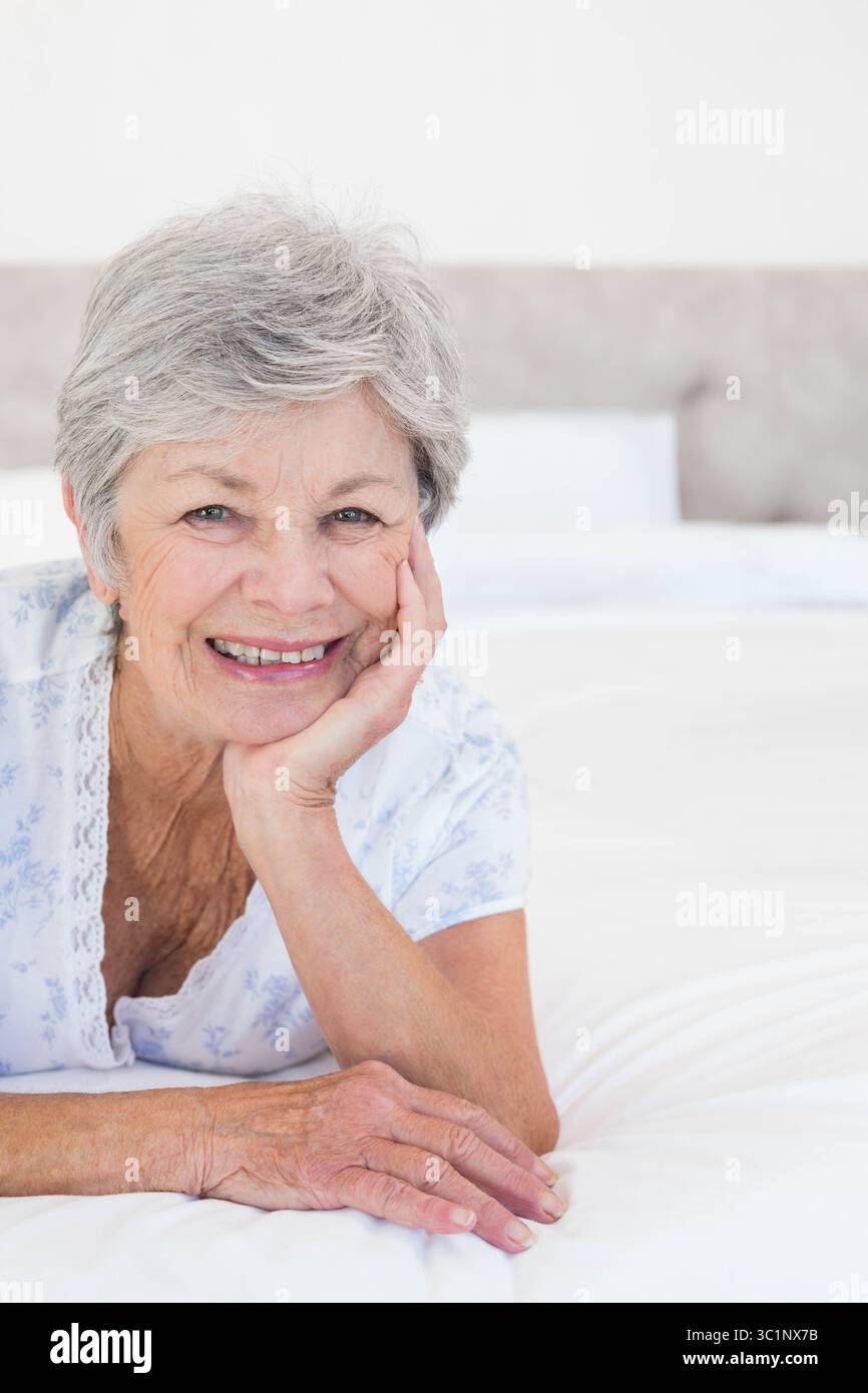 Femme senior couchée sur le ventre sur le lit dans la chambre, portant le dessus floral et reposant sur le coude Banque D'Images