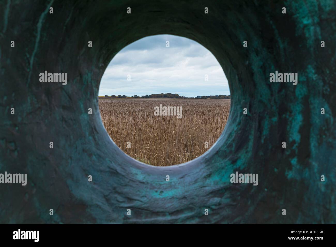 Vue à travers une ouverture circulaire dans une sculpture, encadrant un champ rural et créant une perspective unique entre l'art et le paysage. Banque D'Images
