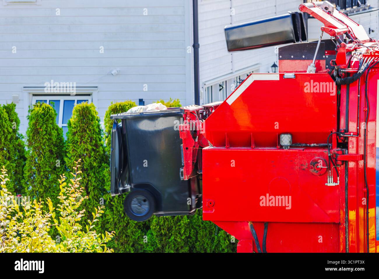 Poubelle noire soulevée par camion à ordures rouge automatisé dans la zone de villa européenne. Suède. Banque D'Images